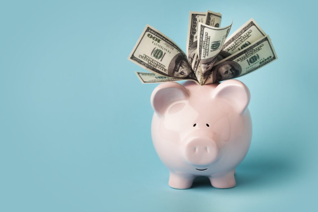 "A smiling pink piggybank stuffed with $100 dollar bills, on blue background with copy space.  You may also like:"