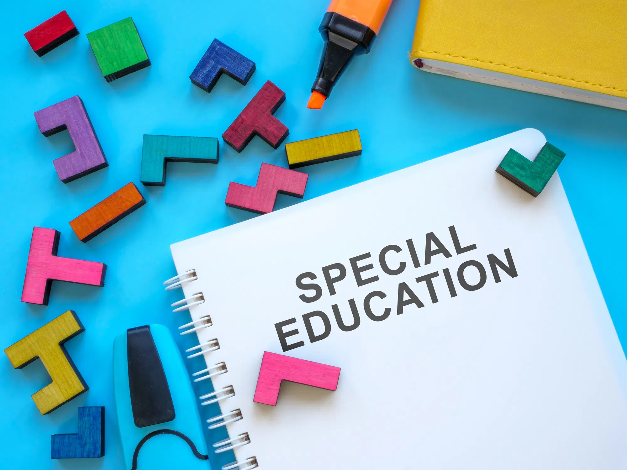 Spiral notebook labeled "Special Education" surrounded by colorful wooden puzzle pieces, an orange marker, and a yellow bo...