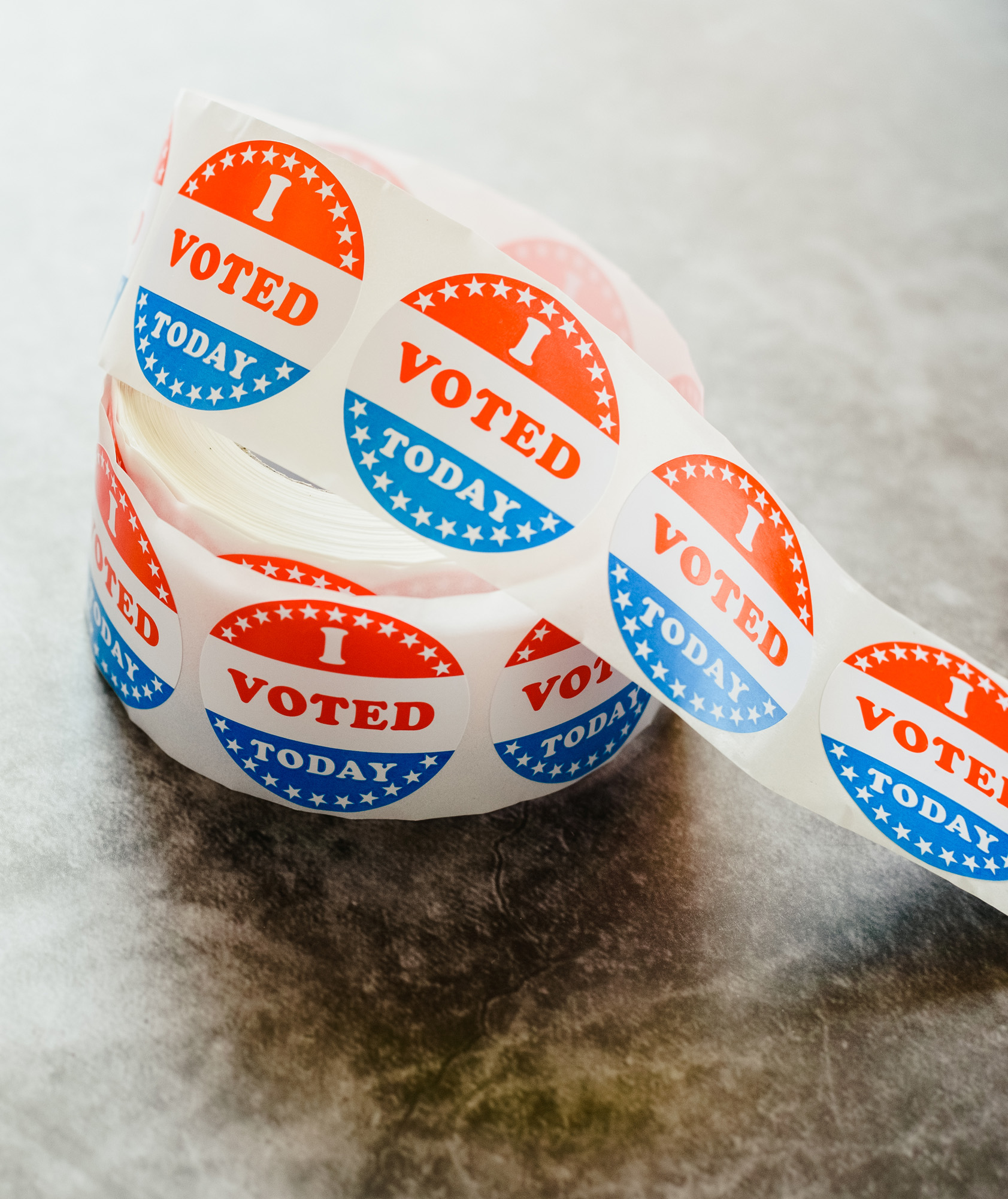 Roll of red, white, and blue circular "I Voted Today" stickers with stars, unrolled on a gray surface.