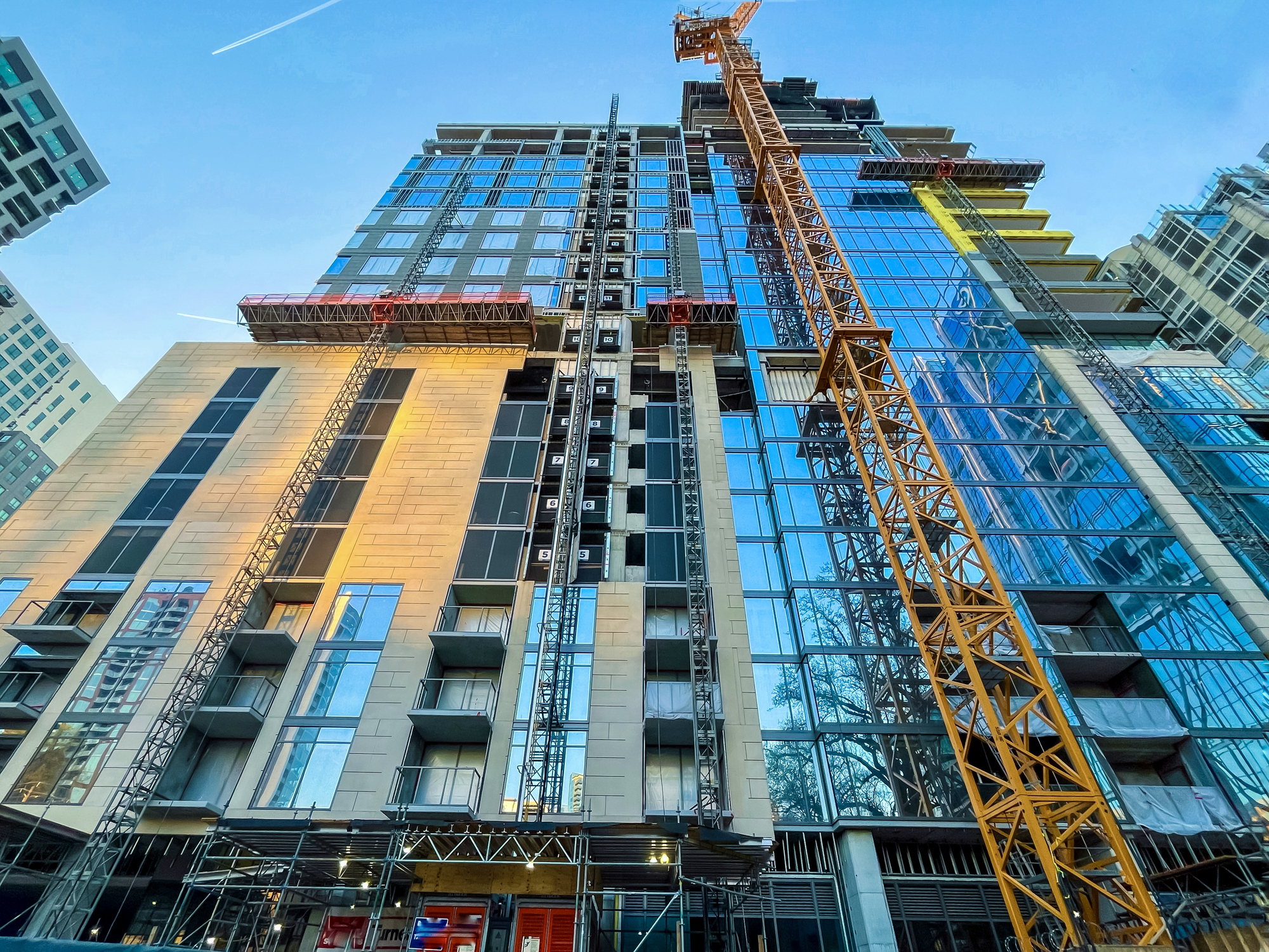Upward view of a high-rise building under construction with yellow tower crane and glass curtain wall facade in urban sett...