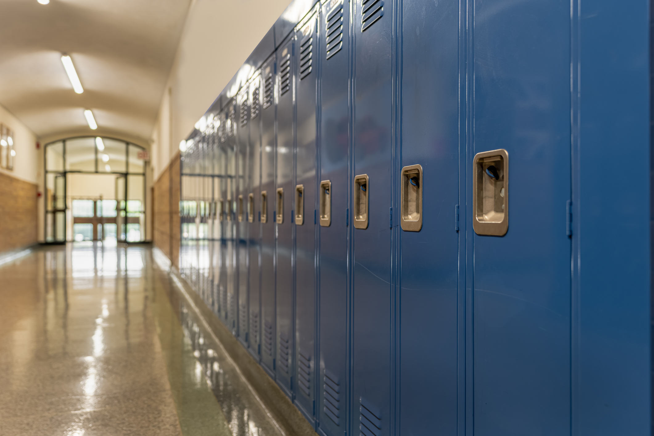 Row of blue metal school lockers lining an empty hallway with polished floors and arched windows at the far end