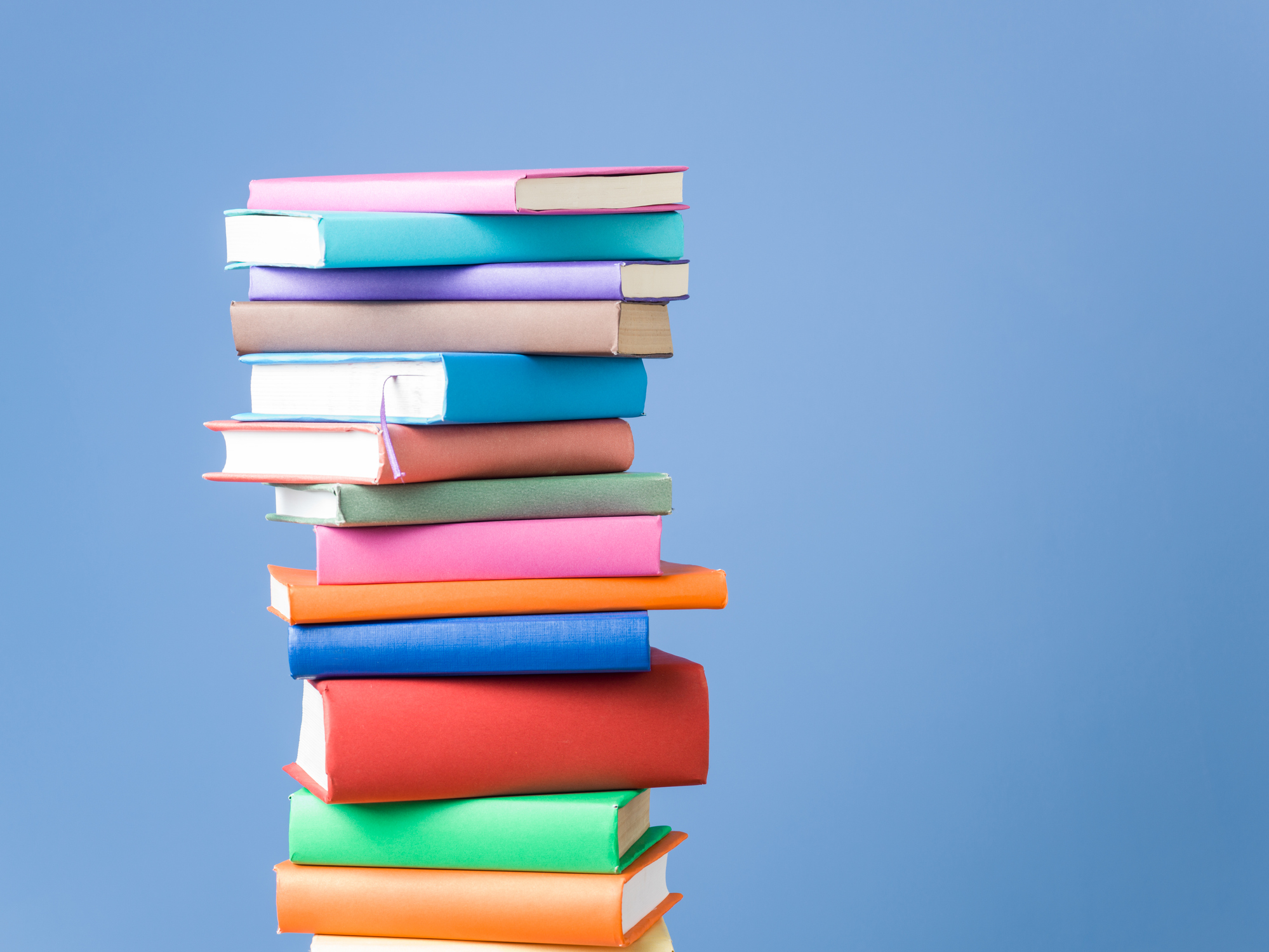 Tall stack of colorful hardcover books in pink, blue, red, green, and orange against a light blue background