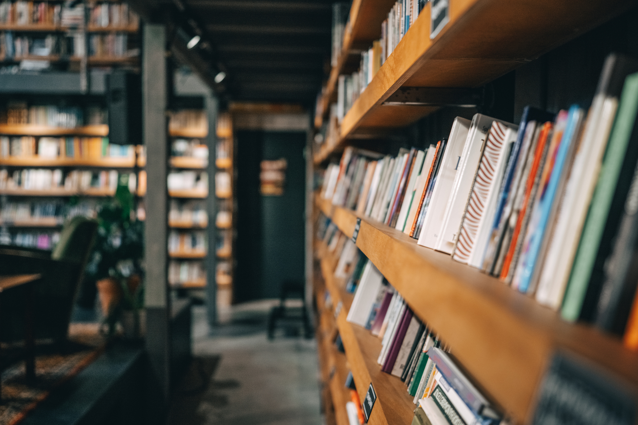 Narrow aisle in a cozy bookstore or library with tall wooden shelves filled with books and a reading chair in the background