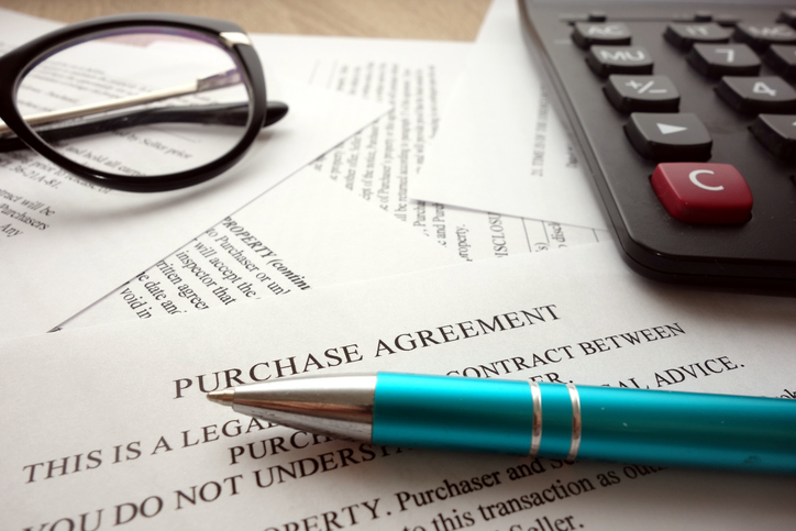Purchase Agreement document with a teal pen, black-rimmed glasses, and calculator on a wooden desk