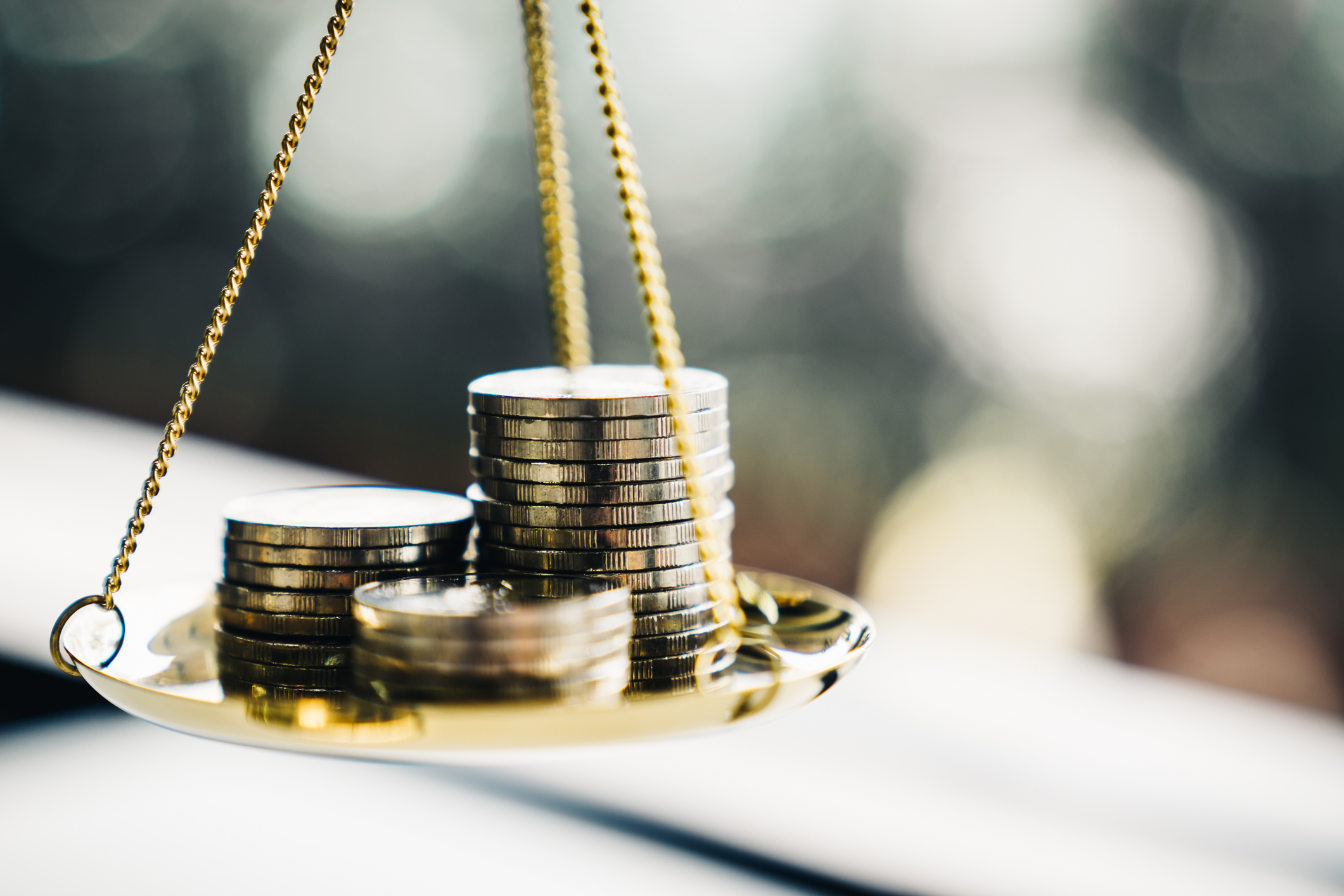 Three stacks of silver coins on a gold balance scale pan, symbolizing financial justice or monetary value judgment