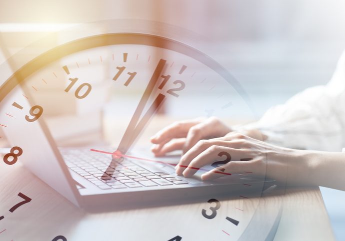 Person typing on a laptop keyboard overlaid with a transparent analog clock face, symbolizing time management or deadlines