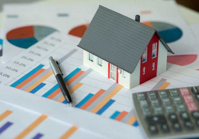 Miniature red and white house model on financial charts and pie graphs, with a pen and calculator, representing real estat...
