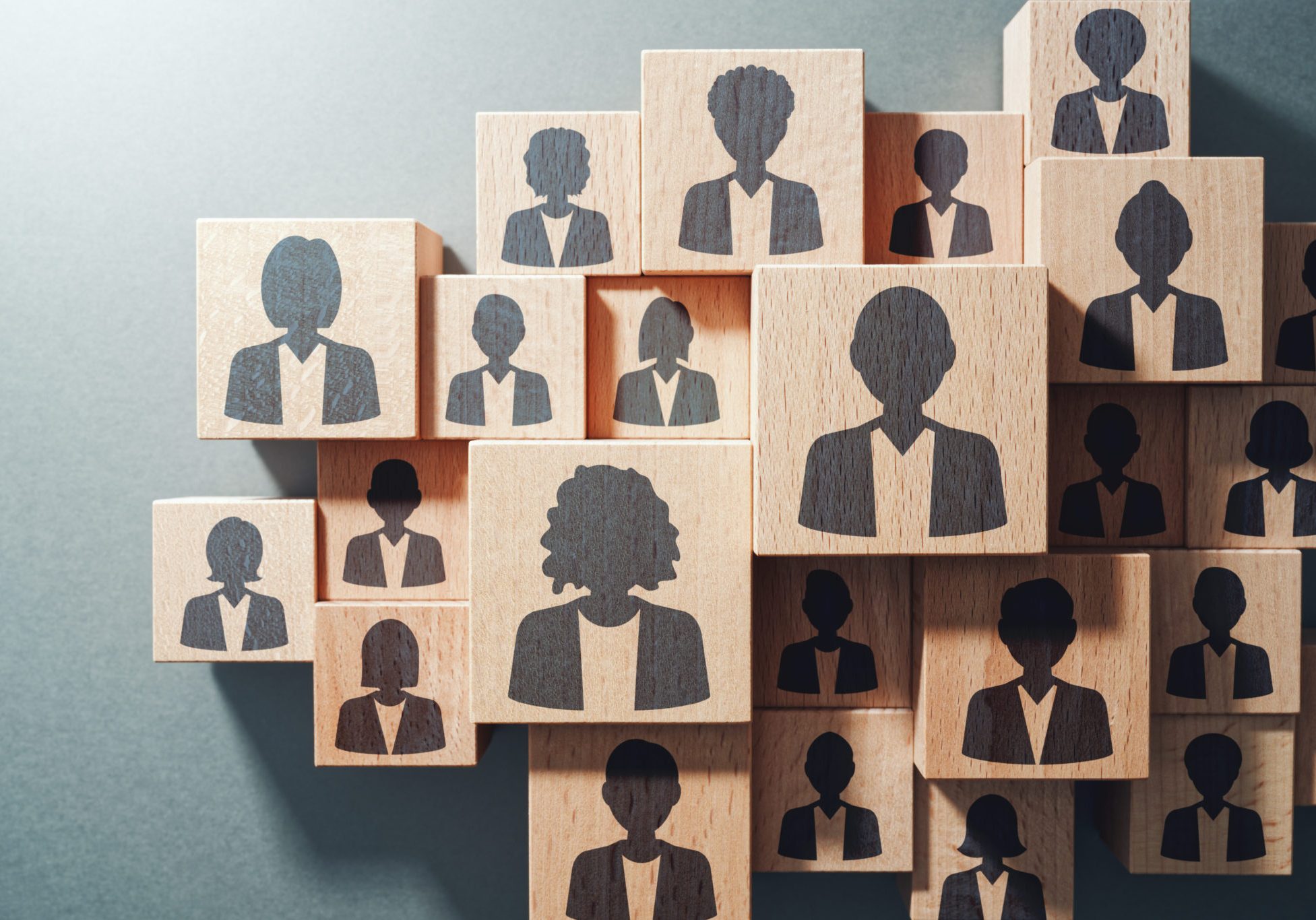 Wooden blocks arranged in a group, each stamped with a dark silhouette icon of a different person in business attire, repr...