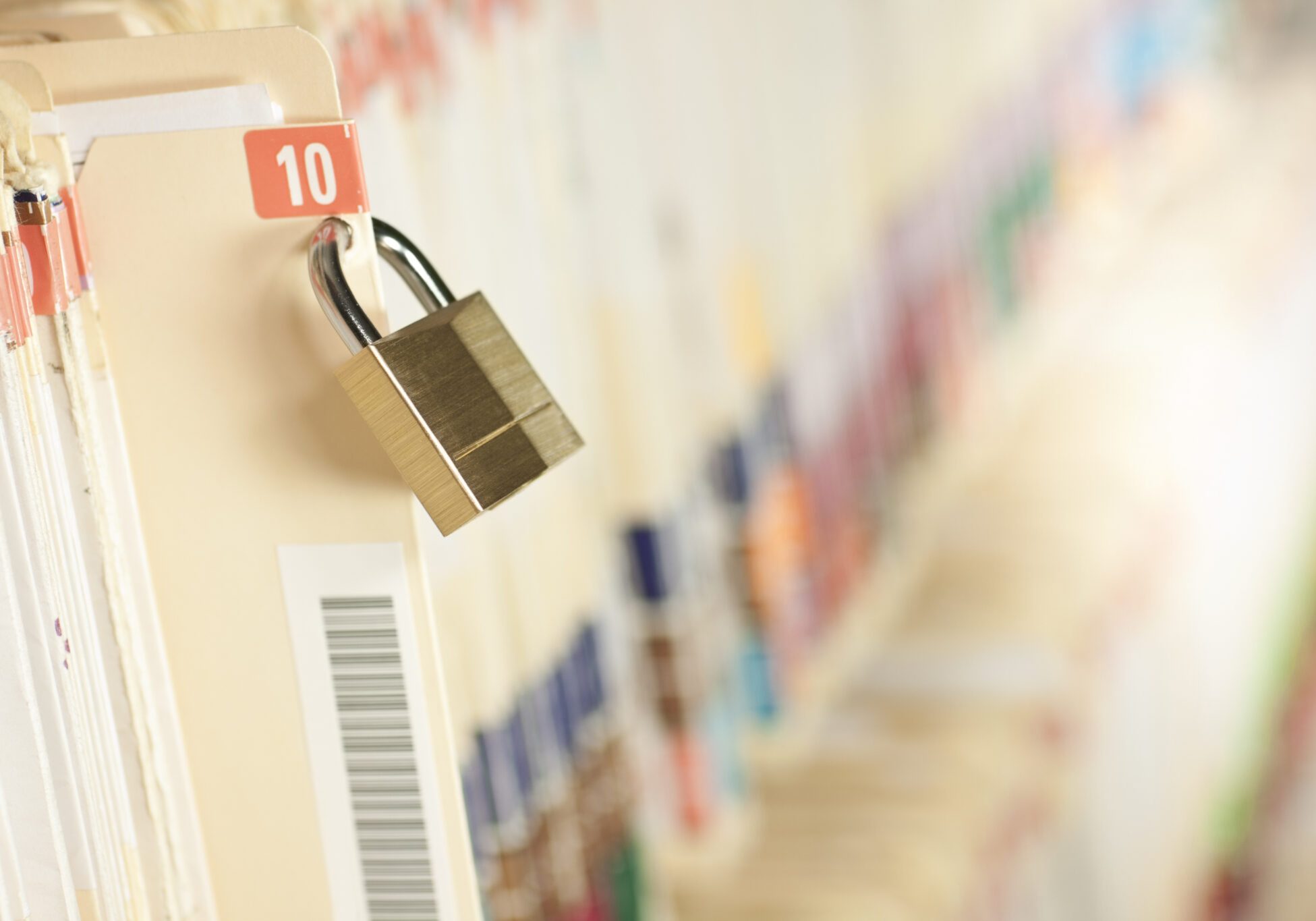 Brass padlock securing a row of medical filing folders labeled with a red number 10 tab and barcode sticker