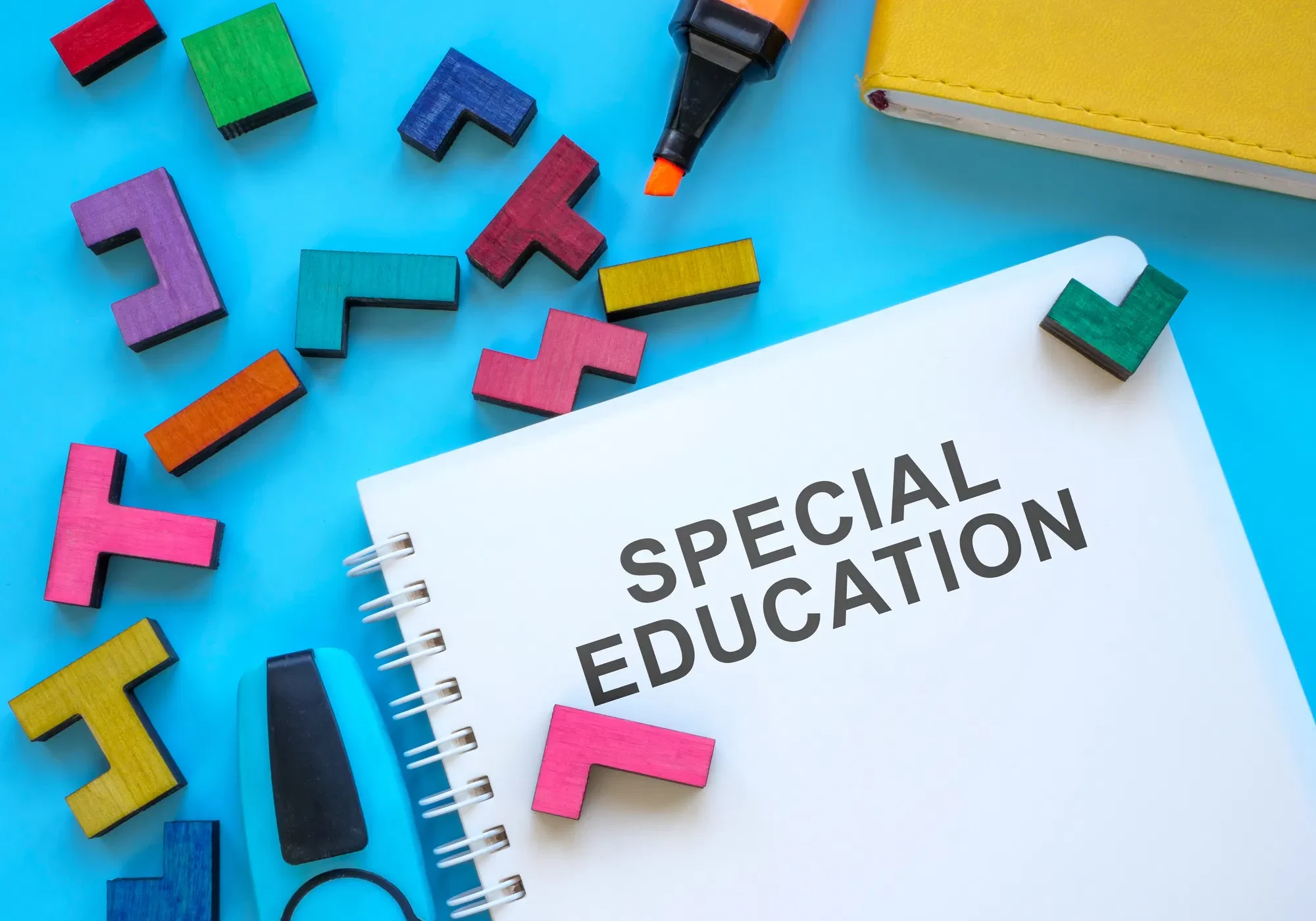 Spiral notebook labeled "Special Education" surrounded by colorful wooden puzzle pieces, an orange marker, and a yellow bo...