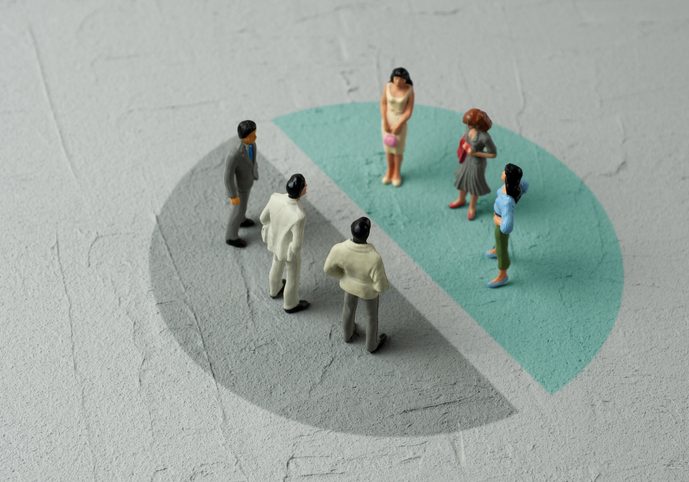 Miniature figurines of people standing on a painted pie chart divided into gray and teal segments, representing demographi...