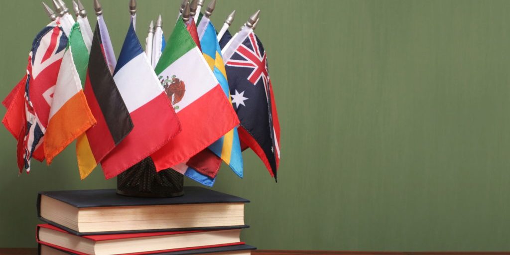 Cluster of small international flags including Mexico, Australia, UK, and Germany displayed on a stack of books against a ...