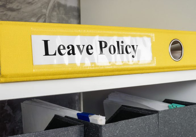 Yellow binder labeled "Leave Policy" on a shelf above gray document organizer boxes with files inside
