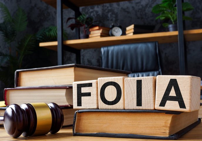 Wooden letter blocks spelling FOIA on stacked law books beside a judge's gavel in a law office setting
