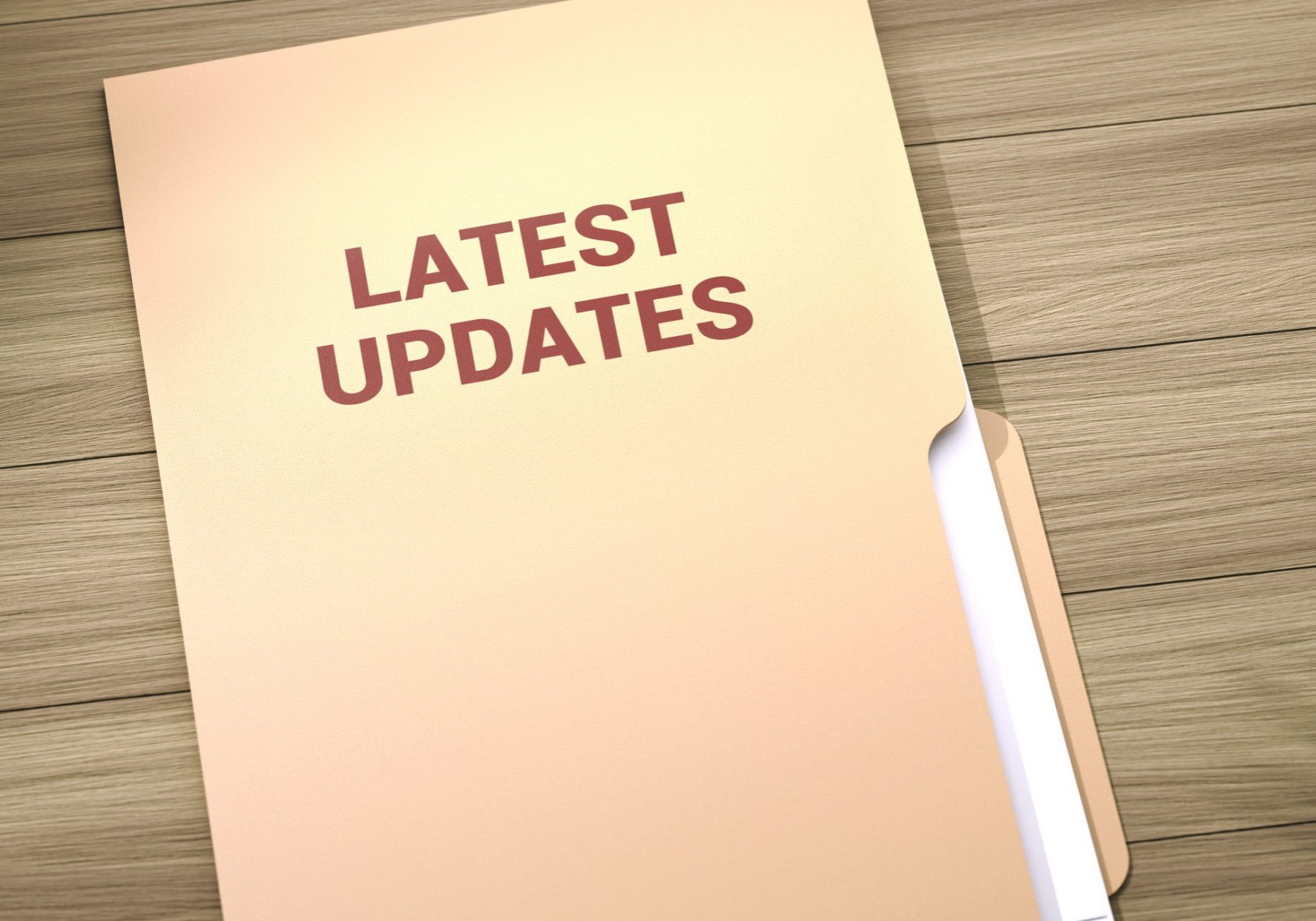 Beige manila folder labeled "LATEST UPDATES" in bold red text, lying on a wooden desk surface with a document inside.