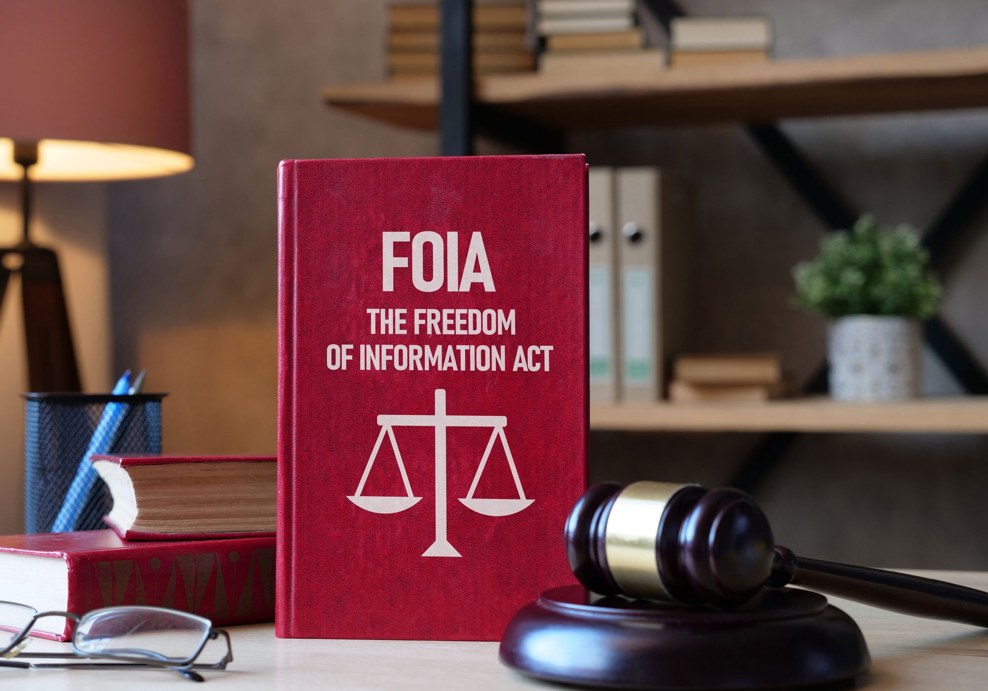 Red book titled FOIA The Freedom of Information Act with scales of justice icon, beside a wooden gavel on a desk