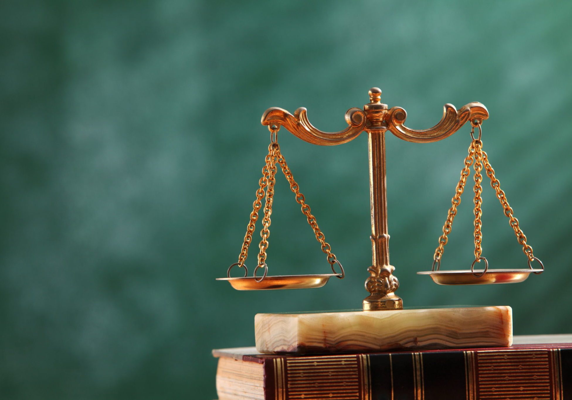 Brass scales of justice balanced on a marble base atop old law books against a green background