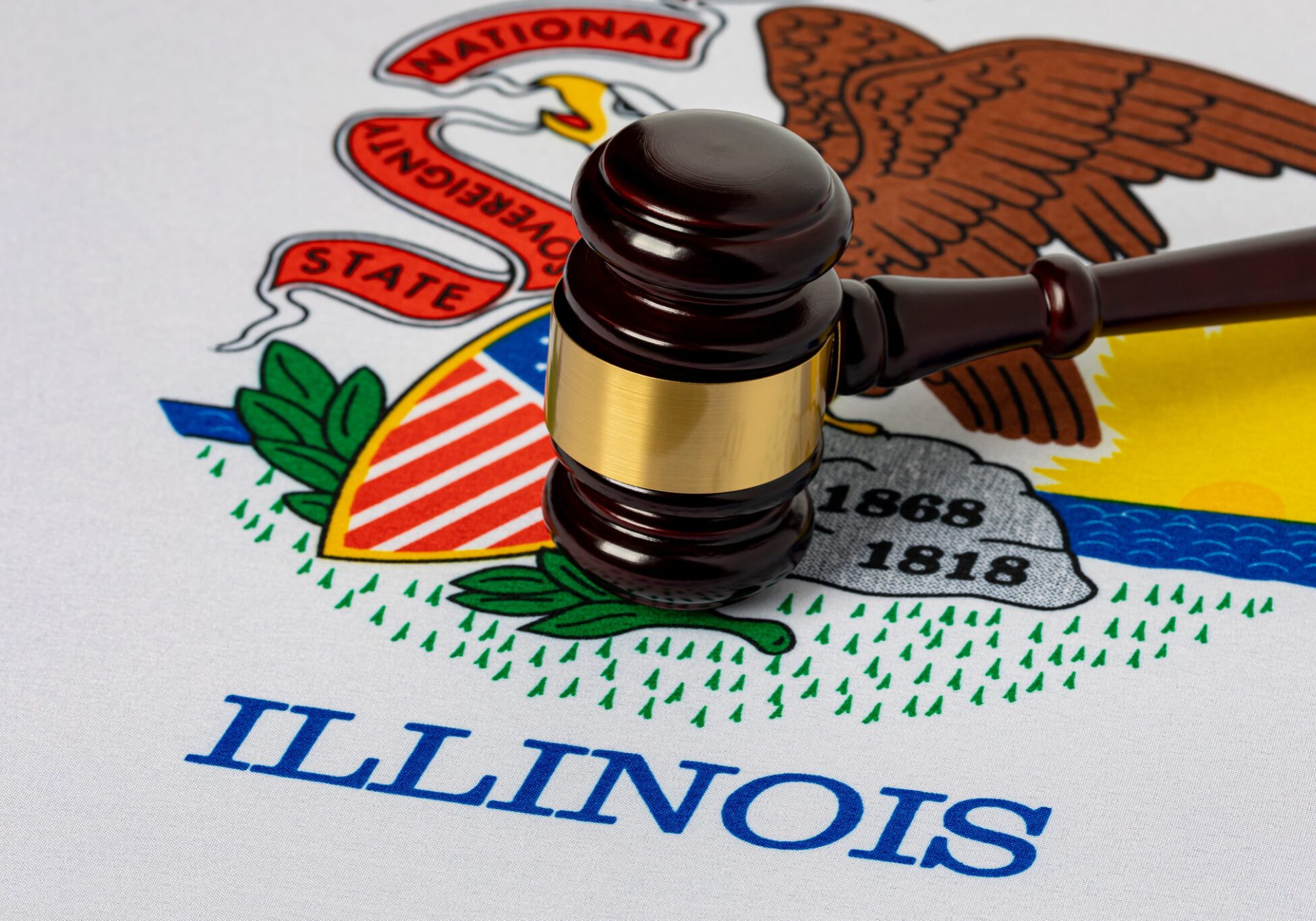 Wooden judge's gavel resting on the Illinois state flag featuring the state seal, eagle, and the word ILLINOIS in blue text