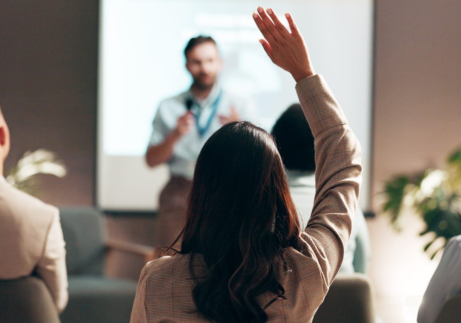 Business people, seminar and convention with audience, question and interaction for feedback or engagement. Group, speaker and back of employee with hand raised for proposal or speech at presentation