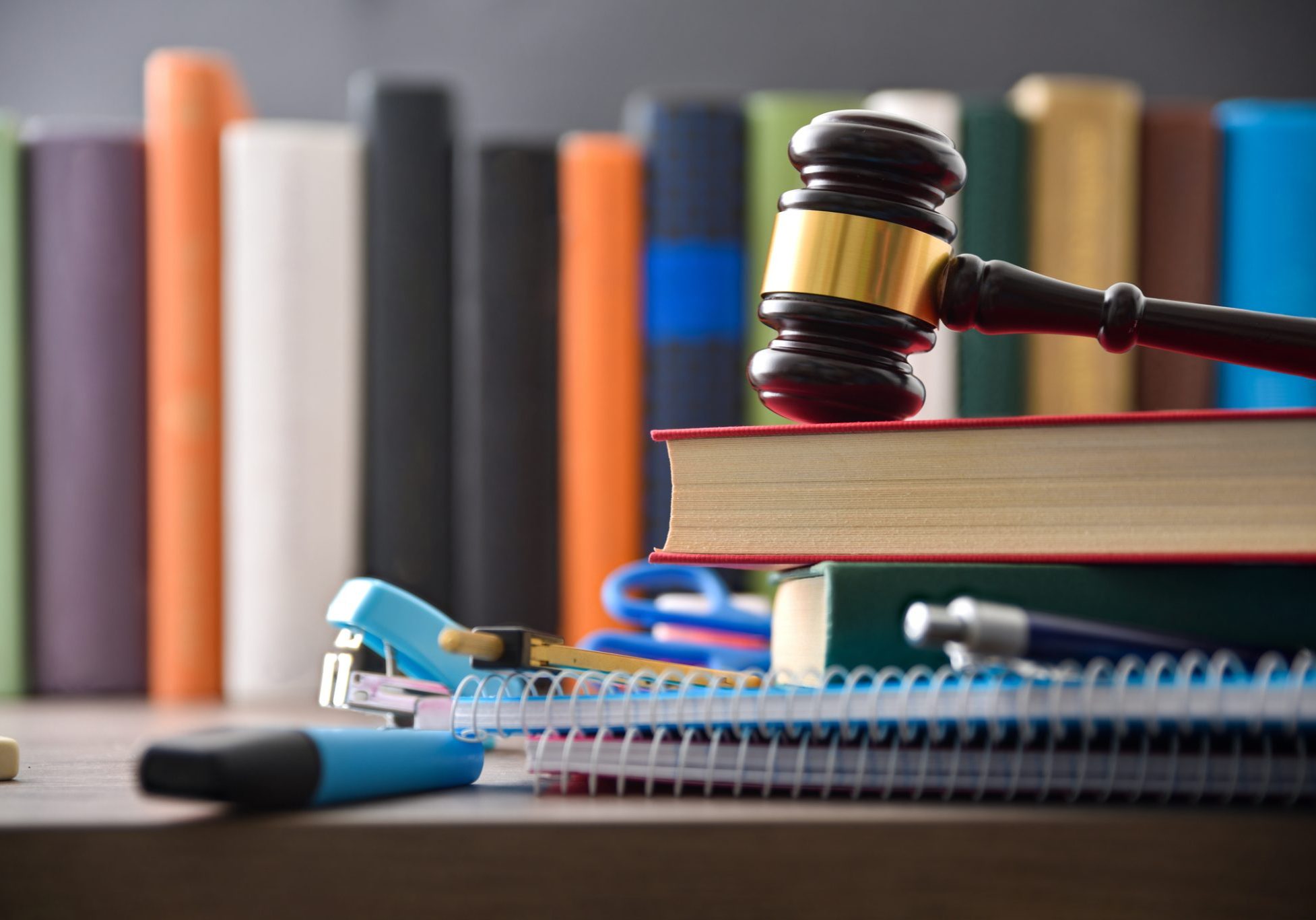 Concept of the right to education with school supplies and a judge's gavel on top of a wooden table and a row of textbooks in the background. Front view.